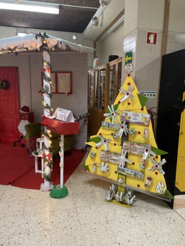 Árvore Natalícia amarela enquadrada no hall de entrada da escola, juntamente com outros trabalho de decoração de Natal realizados pelos alunos com materiais reutilizados.