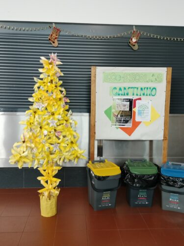 Árvore de Natal Amarela colocada no átrio da escola (espaço de convívio dos alunos) junto ao placard "cantinho Eco-escolas".