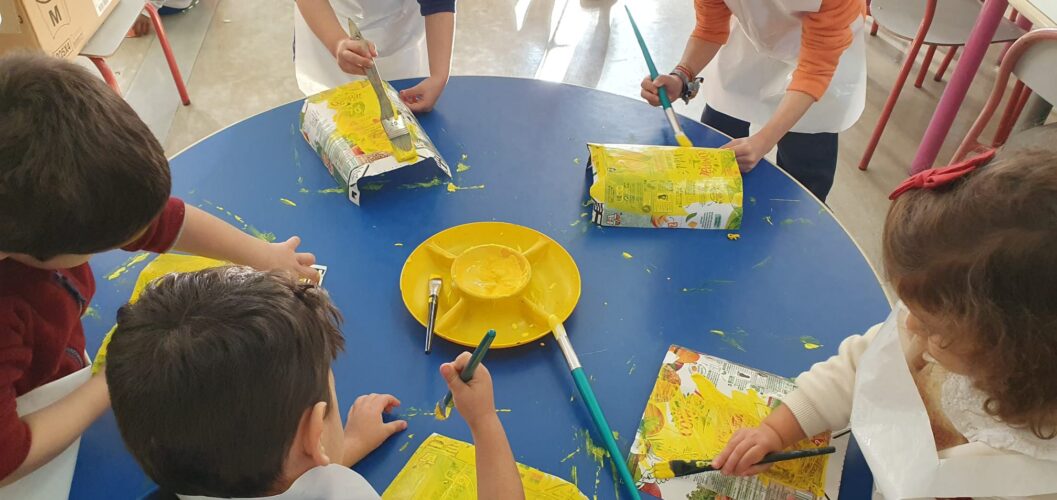 Pintura das embalagens Compal com tinta amarela pelas crianças