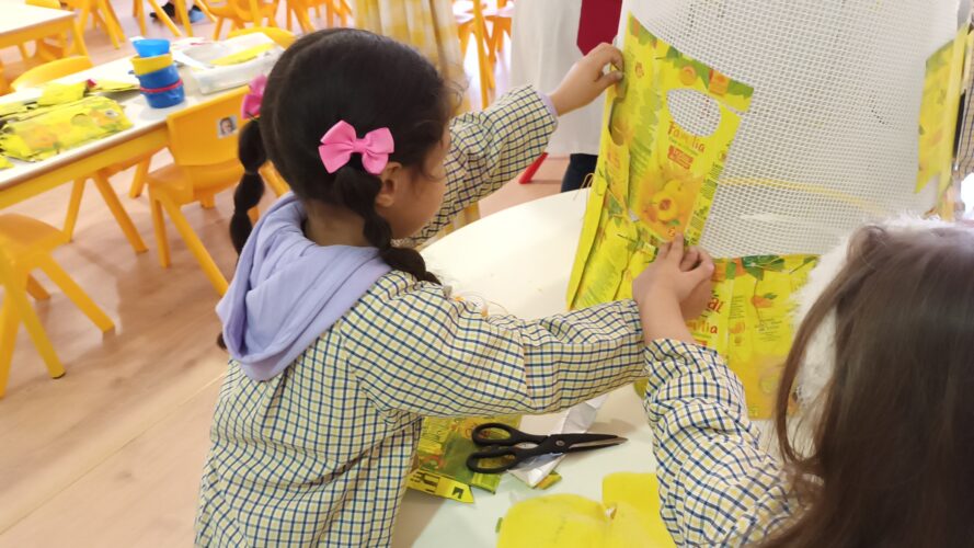 As crianças colocaram as embalagens Tetra Pak pintadas de amarelo na estrutura de rede. Umas foram penduradas e atadas com fios usados e outras agrafadas. - foto " colocação das embalagens"
