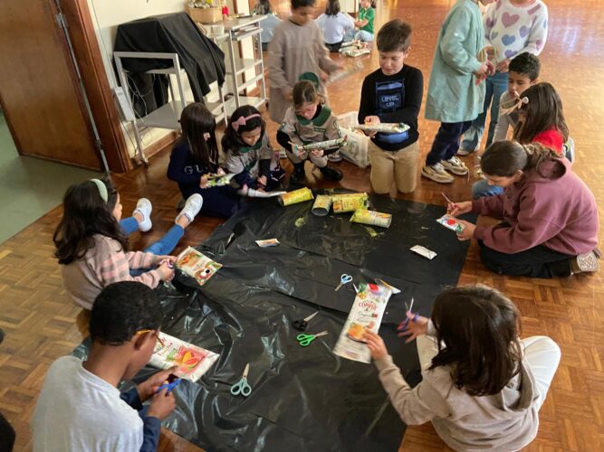 As crianças em momento de exploração e construção da Árvore de Natal, utilizando as embalagens e colaborando em grupo.