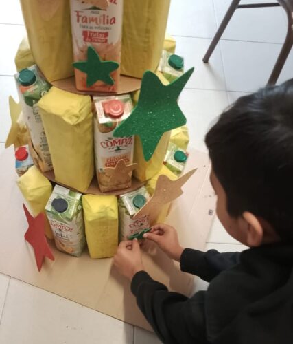 Aluno a decorar árvore com EVA´s brilhantes coloridas, recortadas previamente em forma de estrela.