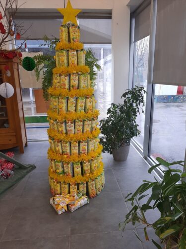 A Árvore de Natal foi colocada no átrio de entrada da escola. Colocaram-se as embalagens Compal que restaram como se fossem presentes junto à árvore.