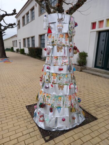 Árvore de Natal Sustentável - decorada com materiais reutilizados, com estrutura em forma de cone a envolver o tronco, composta por camadas de embalagens de leite e sumo Compal, criando um efeito orgânico e criativo, e com elementos decorativos.