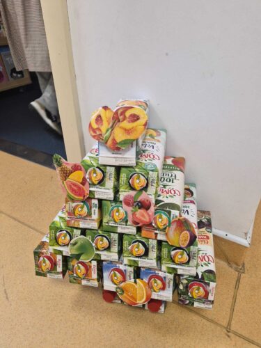 Durante a construção da Árvore de Natal, é possível identificar claramente a utilização de embalagens da marca Compal, cuja presença se destaca pelas cores e padrões característicos. Em várias partes da estrutura observam-se superfícies onde surge o logót