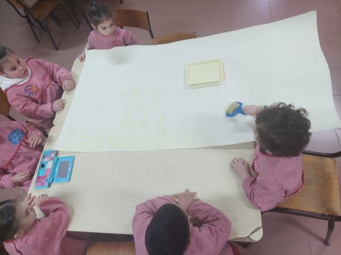 Crianças do pré-escolar a pintar o fundo do painel.