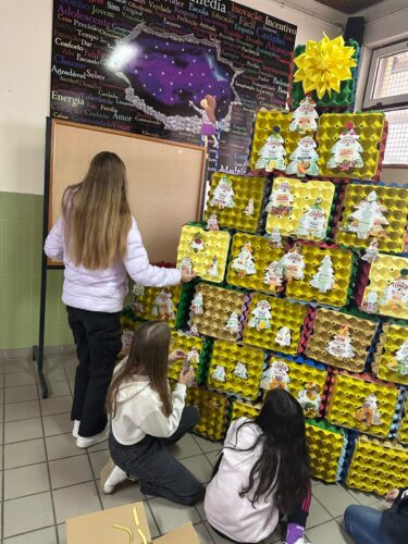 Colocação dos enfeites de natal elaborados com as embalagens da marca Compal na árvore de natal (construída com cubos elaborados com caixas de ovos).