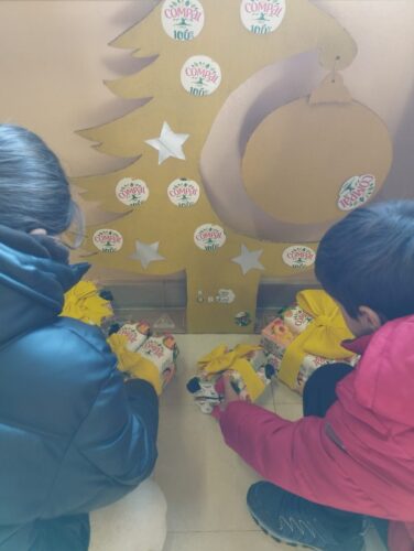 Montagem do trabalho final com a árvore pintada de amarelo decorada com motivos recortados de pacotes de compal (interior prateado e exterior) e prendas feitas com embalagens de compal e decoradas com laços amarelos.