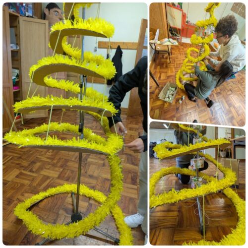 Montagem da estrutura da árvore<br/>Como base, usou-se um suporte de microfone. Apoiado nesse suporte, colocou-se uma espiral de cartão reutilizado (preso com cordéis), sobre a qual se colocaram fitas de plástico amarelo, do arraial da Escola do ano anterior