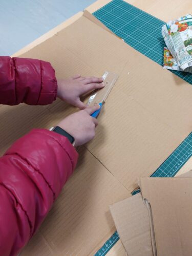 Processo construção_1ª etapa<br/>Para a base do trabalho, utilizou-se cartão proveniente de caixas usadas, sobre o qual foi colada cartolina de cor amarela. Os principais elementos decorativos foram realizados a partir de embalagens Tetra Pak de sumos Compal