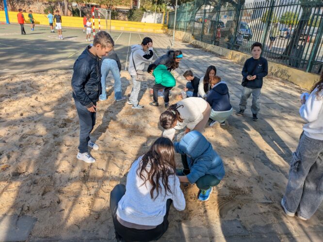 Alunos de 5.º ano a recolher areia da área do local onde se realizam provas de salto na disciplina de Educação Física.